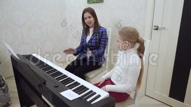 年轻的老师和小可爱的女孩在电动钢琴上演奏。